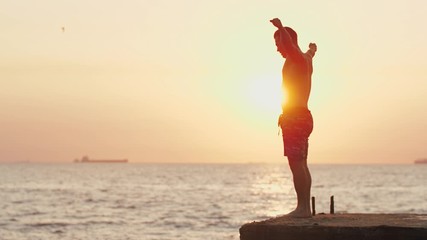 Young man jumping from sea pier and doing frontflip during beautiful sunrise, slow motion
