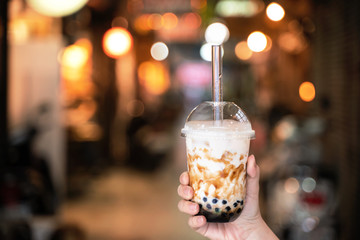 Young girl in denim jacket is drinking brown sugar flavored tapioca pearl bubble milk tea with...