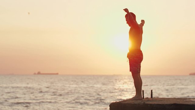 Young man jumping from sea pier and doing frontflip during beautiful sunrise, slow motion