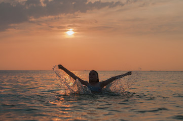 A girl and a water splash with a sunset on the background