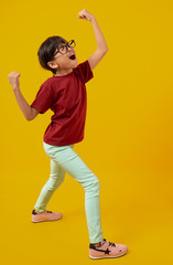 Fototapeta na wymiar Portrait of Asian pretty girl celebrating and raising hand up for successful, Thai kid with glasses in red shirt have glad and joy on yellow in studio