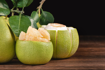 Fresh peeled pomelo, grapefruit, shaddock with green leaves on dark wooden plank table. Seasonal...