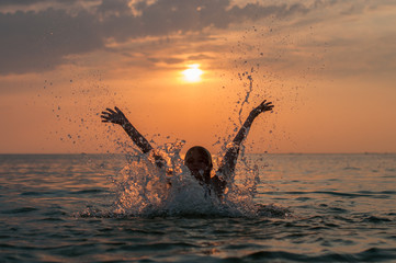A girl and a water splash with a sunset on the background