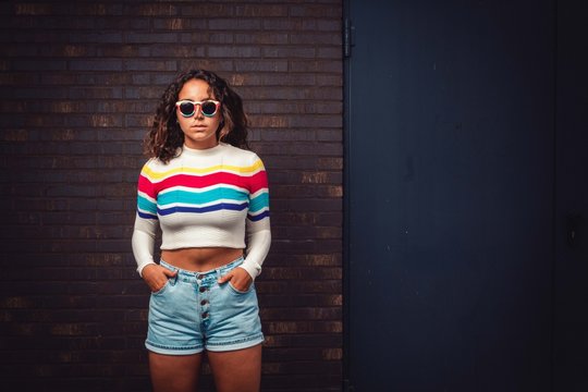 Curly haired woman with colored sunglasses infront of brick wall