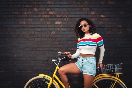 Dark haired girl on bycicle infront of brick wall