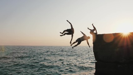 Group of young friends jumping and doing tricks from a pier into the sea during beautiful sunrise, slow motion