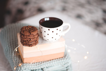 Cup of black tea with chocolate cookies staying on stack of book and knitted sweater closeup in bed. Good morning. Breakfast. Night time.