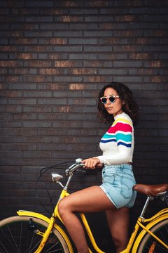 Dark haired girl on bycicle infront of brick wall