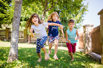 Fototapeta premium Portrait of two girls, sisters and their boy friend running in the park