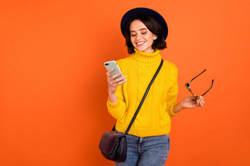 Photo of cheerful nice chatting girl staring at her phone wearing jeans denim walking in autumn while isolated with orange background