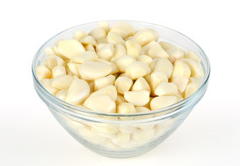 Peeled garlic cloves in glass bowl, front view. Allium sativum, with pungent flavor, used as seasoning or condiment and in medicine. Macro food photo, closeup, on white background.