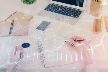 Hands writing information about stock market in notepad. Forex chart holograms in front. Concept of research. Multi exposure