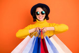Photo of trendy charming excited nice good girlfriend wearing cap holding bags with something newly bought while isolated with orange background