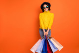 Photo of cute attractive sweet girl wearing jeans denim yellow sweater holding packages customer buyer while isolated with orange background