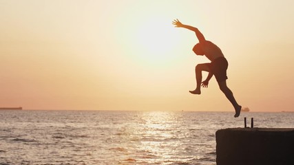 Young man jumping from sea pier and doing backflip during beautiful sunrise, super slow motion
