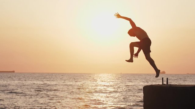 Young man jumping from sea pier and doing backflip during beautiful sunrise, super slow motion