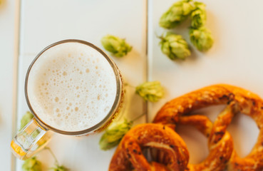  beer mug, hop cones and pretzels on a white wooden table. Oktoberfest background