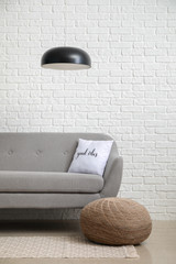 Comfortable sofa and pouf near white brick wall in room