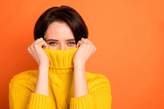 Close up photo of cute nice charming girl hiding from cold by wrapping up in collar while isolated with orange background