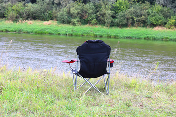 Fototapeta na wymiar Portable folding tourist red armchair on green grass in summer on picnic near river