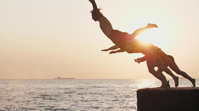 Group of young friends jumping from a pier into the sea, super slow motion
