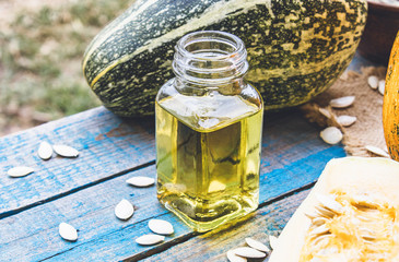 Pumpkin seed essential oil in a bottle near a pumpkin on blue old boards.