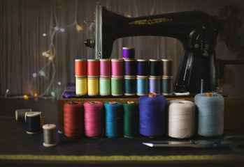 Vintage multicolor sewing threads on dark background of sewing machine, selective shallow focus, sewing supplies