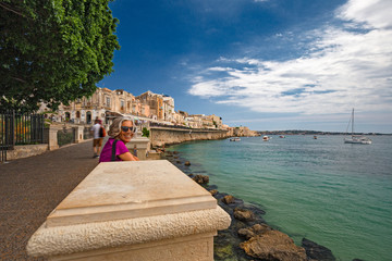 Some tourists walking along the seafront in the historic center of the island of Ortigia in Syracuse, Sicily Italy.