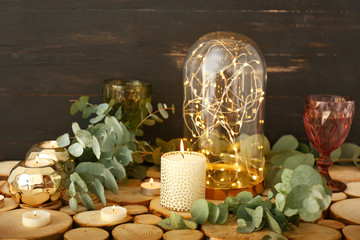 Beautiful burning candles with eucalyptus and glowing garland on table