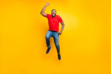 Fototapeta na wymiar Full length body size photo of jumping man wearing red t-shirt jeans denim rejoicing with his victory at something while isolated with yellow background