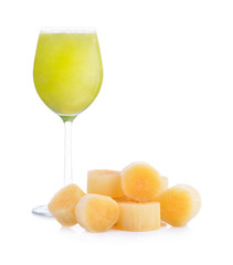 Fresh squeezed sugar cane juice in glass with cut pieces cane on nature background