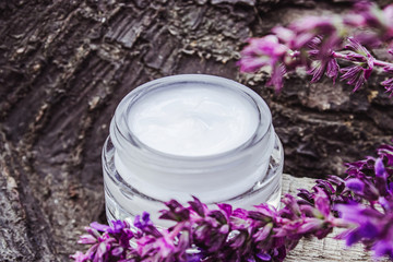 Obraz na płótnie Canvas Cosmetic cream in a glass jar on a wooden background with lavender wildflowers. Face cream.