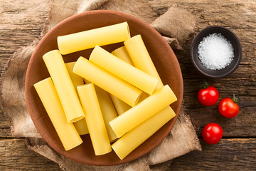 Raw cannelloni pasta on plate, salt and cherry tomatoes on the side, photographed overhead on...
