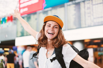 Happy young girl traveler at the airport with a backpack on the background of a departures board