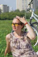 middle-aged woman in sunglasses resting on the lawn in a city park on the background of her bicycle.