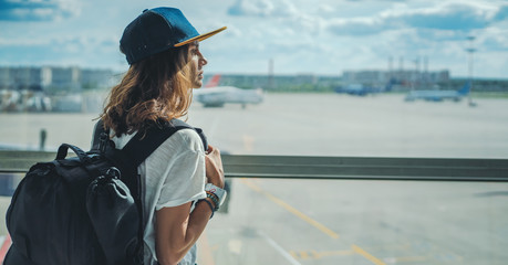 young girl traveler with backpack at the airport on the background of the takeoff field