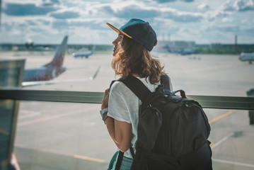young girl traveler with backpack at the airport on the background of the takeoff field