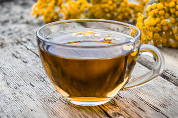 Cup of tea with tansy and tansy flowers on a wooden table. Healing herbs.