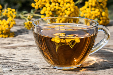 Tansy infusion in a glass cup on a wooden table. Tansy Herbal tea. Healing herbs.
