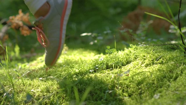 SLOW MOTION, DOF, CLOSE UP: Cinematic shot of a couple's feet hitting the mossy ground during a trail run in the woods. Unrecognizable training partners in new sportswear running along mossy ground.
