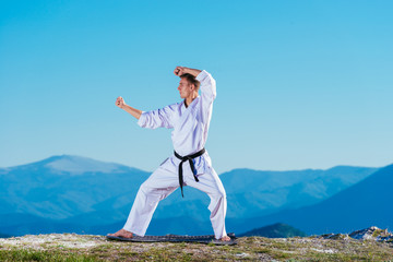 Blond karate athlete does kata on top of a mountain while performing a line up of kicks, punches and blocks on top of a mountain on a sunny day.