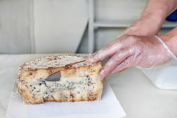 A slice of blue aged delicatessen Stilton cheese on a white table. The seller cuts a piece from the cheese head. Farm quality products