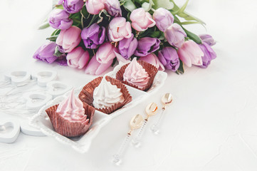 Pink homemade meringues on a white table with a bouquet of pink tulips. Gift set. Copy space