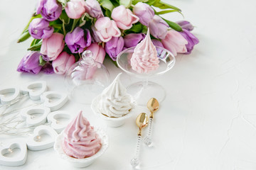 Pink homemade meringues on a white table with a bouquet of pink tulips. Gift set. Copy space