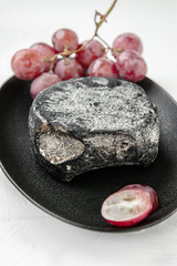 Thurgau is a fine hard Swiss cheese with the aroma of onion bread. Cheese is made in the Canton of Thurgau on lake Constance. A head of cheese with grapes on a black plate