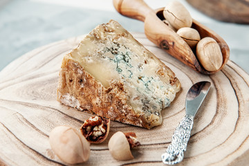 Fototapeta na wymiar A slice of blue aged Stilton cheese on a wooden table. Cheese is served with pecans. Quality of agricultural products of farmers. Delicious English cheeses from Russian farmers