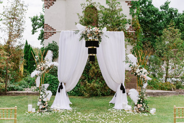 The square arch is decorated with white cloth, black chandelier and fresh flowers.