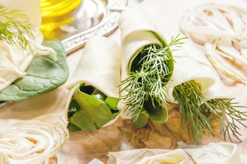 Rolls of thin pancake cheese Suluguni with dill and spinach on a beautiful Board made of natural olive wood. Diet and weight management