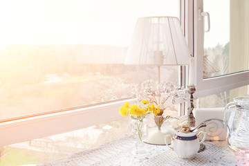 The window of the cafe overlooks the autumn romantic landscape. Interior with lamp and candle on the table with lace tablecloth. Bunch of yellow flowers