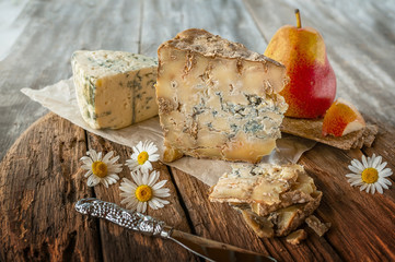 A slice of blue aged Stilton cheese on a wooden table. Cheese is served with a beautiful ripe pear....
